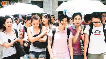 台灣學生躲在傘下，仍難耐炎炎夏日。	（本報台北傳真）