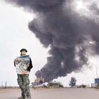 拉斯拉努夫一間冒煙的煉油廠前，有政府軍士兵拿着卡達菲的肖像表示忠誠。		（美聯社圖片)