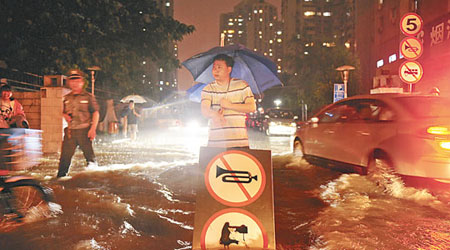 北京暴雨導致市內嚴重水浸，車輛行人涉水而行。（中新社圖片）