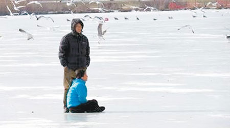 華裔婦跑到結冰湖泊坐下，丈夫在旁勸說。（互聯網圖片）