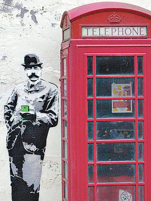 電話亭旁的埃爾加爵士右手插袋，左手持智能電話。（互聯網圖片）