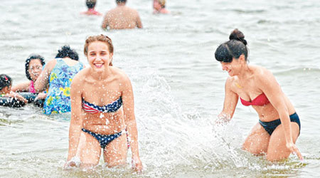 夏日炎炎，有外國遊客在沙灘戲水消暑。（中新社圖片）