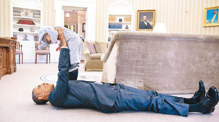 奧巴馬躺在白宮辦公室地上，抱起幕僚的女兒逗玩。（白宮圖片）