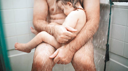 托馬斯（後）摟着兒子（前），坐在浴室一角淋浴。