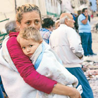 女災民一臉擔憂，抱着孩子站在街邊。