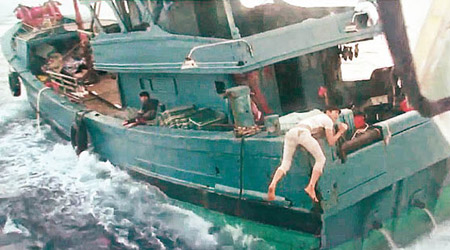 一名漁民半個身體懸在船邊，險象環生。