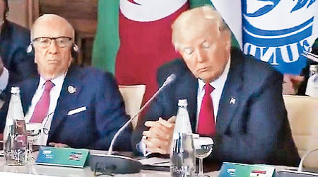 特朗普出席G7峰會時再爆出笑料，他在東道主意大利總理真蒂洛尼發言時，沒戴上傳譯耳機，卻裝出一副正在聽的樣子（右）。（電視畫面）