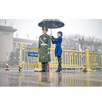昨日北京下雪，一名女職員在會場外為軍警撐傘。