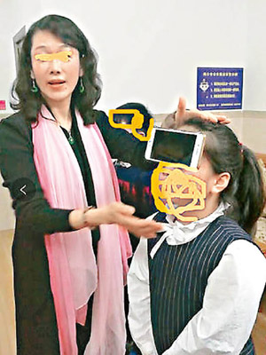 何女（左）展示孩子用額頭「控制」手機。（互聯網圖片）