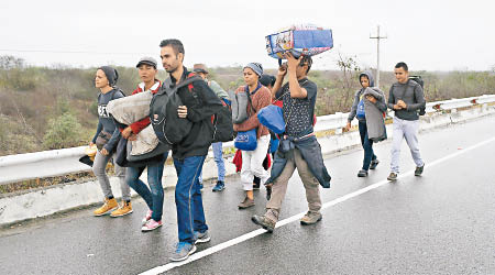 難民托着行李在公路上徒步前行。（美聯社圖片）