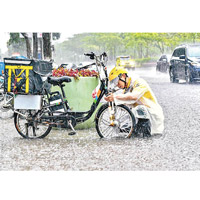 廣州<br>廣州街頭水浸，外賣員在積水中修理電動車。（中新社圖片）