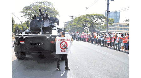 一名示威者手持標語站在裝甲車前方。（美聯社圖片）