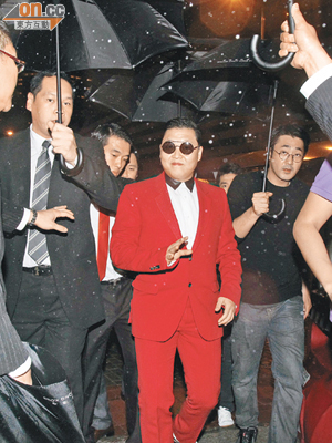 一身紅色西裝的Psy由多位工作人員撐傘擋雨，十分架勢！
