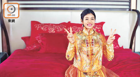 穿上「橘色鳳彩裙褂」的陳妍希坐在紅噹噹的床上，舉起幸福勝利手勢。