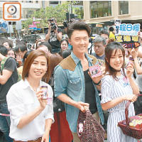 宣萱（左起）、王浩信和唐詩詠在中環派紀念品，被大批上班族包圍。