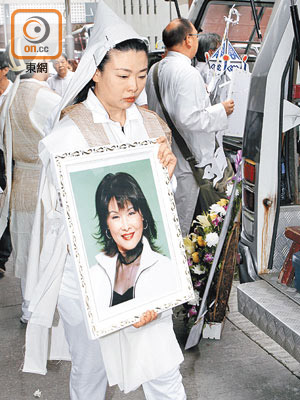 廖麗麗女兒捧着遺照步出殯儀館。