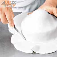 把糖粉糰壓平為薄皮，整塊蓋在蛋糕上，切走多餘部分。