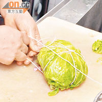 最後以椰菜葉將層層疊的椰菜豬肉包裹成一個球狀，用繩將其綁好。