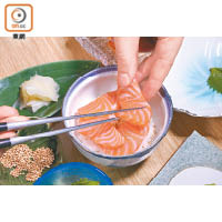在壽司飯上灑上預先用白鑊炒香的芝麻，然後圍着碗邊鋪上4片三文魚刺身。
