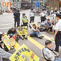 多名警員勸導坐在馬路中央的雷曼苦主離開該段危險區域。	（梁耀榮攝）