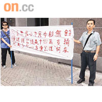 事主姚耀華（右）由友人陪同，在馬會總部大樓外拉橫額抗議。	（陳桂建攝）