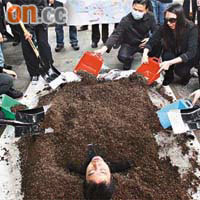 區議員陳岳鵬以沙泥「活埋」自己，抗議南港島線工程在鋼線灣設置卸泥區。（陸智豪攝）