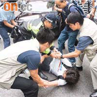 民間電台FM101成員突然躺在馬路上，圖阻擋唐英年座駕離開，最後被警方抬走。