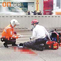 鐵騎士翻車後撞向巴士，重傷倒臥路中，救護員為他急救。	（讀者提供圖片）