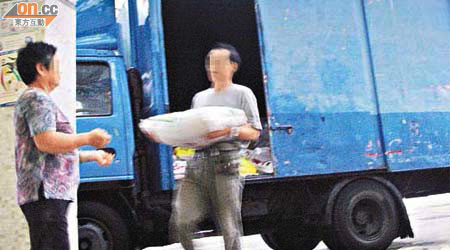 貨車司機在貨車內抬出一包約二十公斤白米交貨。