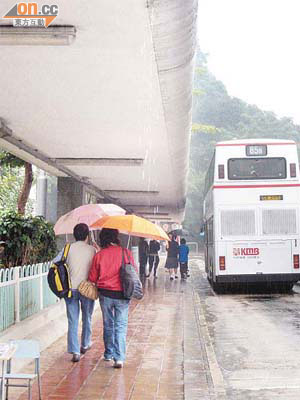 巴士總站弧形上蓋令雨水滿溢便一瀉而下，途人只好在「有瓦遮頭」下撐傘避雨。