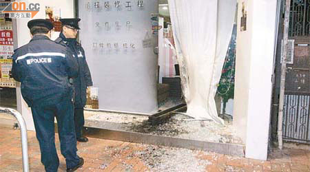 警員在縱火案現場調查，門框熏黑，大門玻璃碎散滿一地。	（楊偉嶽攝）
