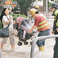 食水湧出，工人協助女士提嬰兒車過路。	（馬竟峯攝）