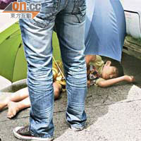 墮樓男童重傷倒臥小巴車旁，途人為他打傘遮擋陽光。	（甄國亮攝）