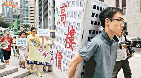 遊行人士背負象徵地產霸權的大廈紙紮模型，意指市民淪為房奴。	（翁志偉攝）