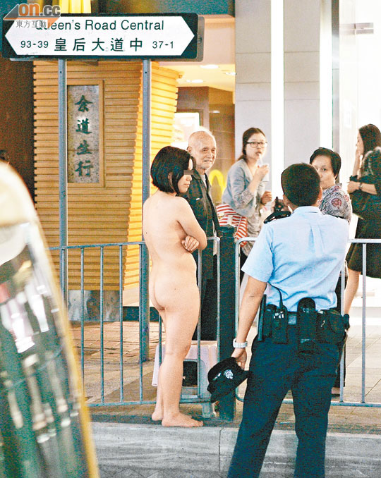 裸女站在街頭以手遮掩胸部。