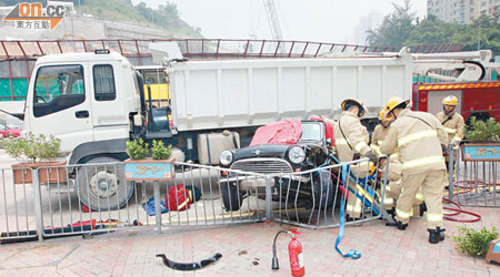 私家車被夾在泥頭車與路邊鐵欄之間，場面驚險。（林少兒攝）