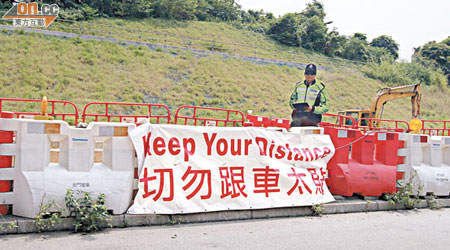 鋁警在粉嶺公路路旁站崗，旁有橫額呼籲駕駛者勿跟車太貼。（陳錦輝攝）