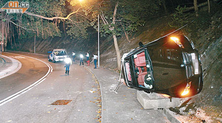 跑車翻側擱在沙井上，天窗開啟，警員在現場調查。（呂浩鋒攝）