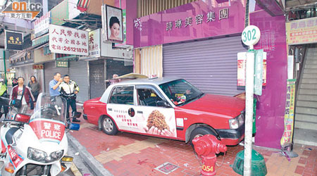 的士剷上行人路，撞向美容店捲閘門邊。（王偉安攝）