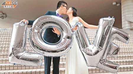 張先生及太太手持寫着「LOVE」吹氣字樣，熱吻賀新婚。（陸建宏攝）