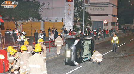 七人車翻側橫擱路中，車身損毀，消防員在場戒備。（賴南秋攝）