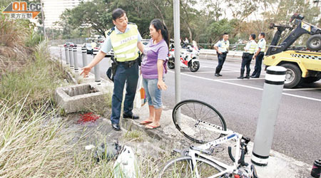 目擊車禍的女傭在場協助警方調查，肇事單車翻側在鐵柱旁。（高潤榮攝）