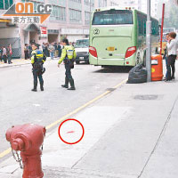 肇事旅遊巴停在路旁，消防栓旁留下一攤血漬（圓圈示），警員在場調查。（左錦鴻攝）
