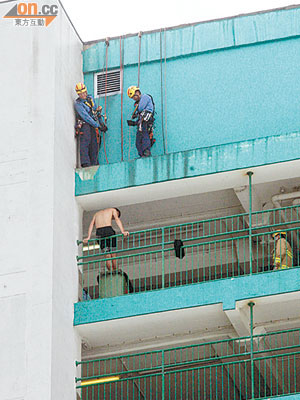 青年坐在欄杆上圖跳樓，消防員「飛將軍」在對上簷篷伺機援救。（何仲軒攝）