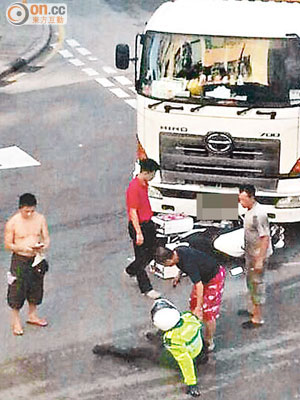 泥頭車撼電單車，警員受傷坐在地上，熱心途人上前協助。（讀者溫政文提供）