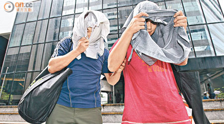 男被告戴志偉（左）和女被告區玉珊（右）否認八項控罪，以衣物遮掩樣貌離開區域法院。