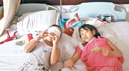 小斌斌和姐姐終於重聚，二人躺在病床上吃零食。（中新社圖片）