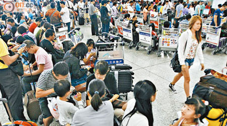 機場各航空公司辦理登機櫃位前排滿團團轉的旅客。（伍鎮業攝）