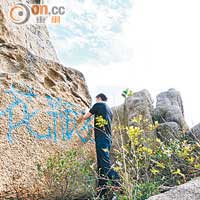 義工Alex爬上陡峭的岩石，手執沙紙狂刷石。
