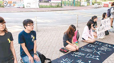 約十名中文大學學生昨在大學港鐵站對出，下跪排成一線，地上橫額寫有「我們被迫擾亂民生，只因本就民不聊生」。（中大學生報相片）